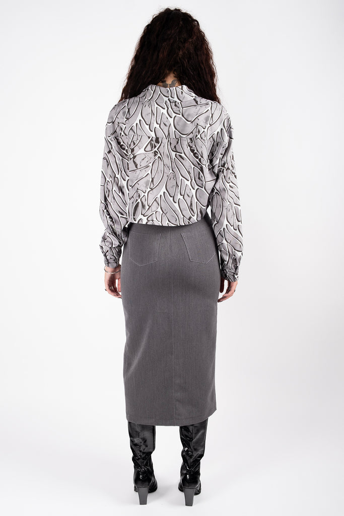 Person wearing a patterned blouse and gray skirt on a white background