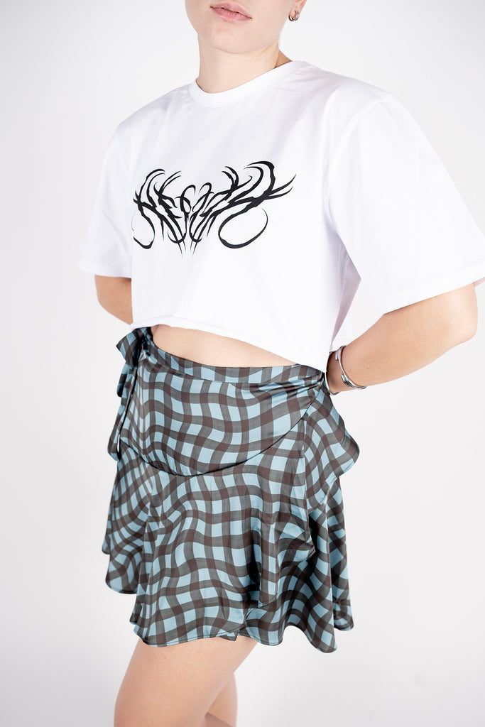 Person wearing a white t-shirt with black graphic design and a plaid skirt on a white background